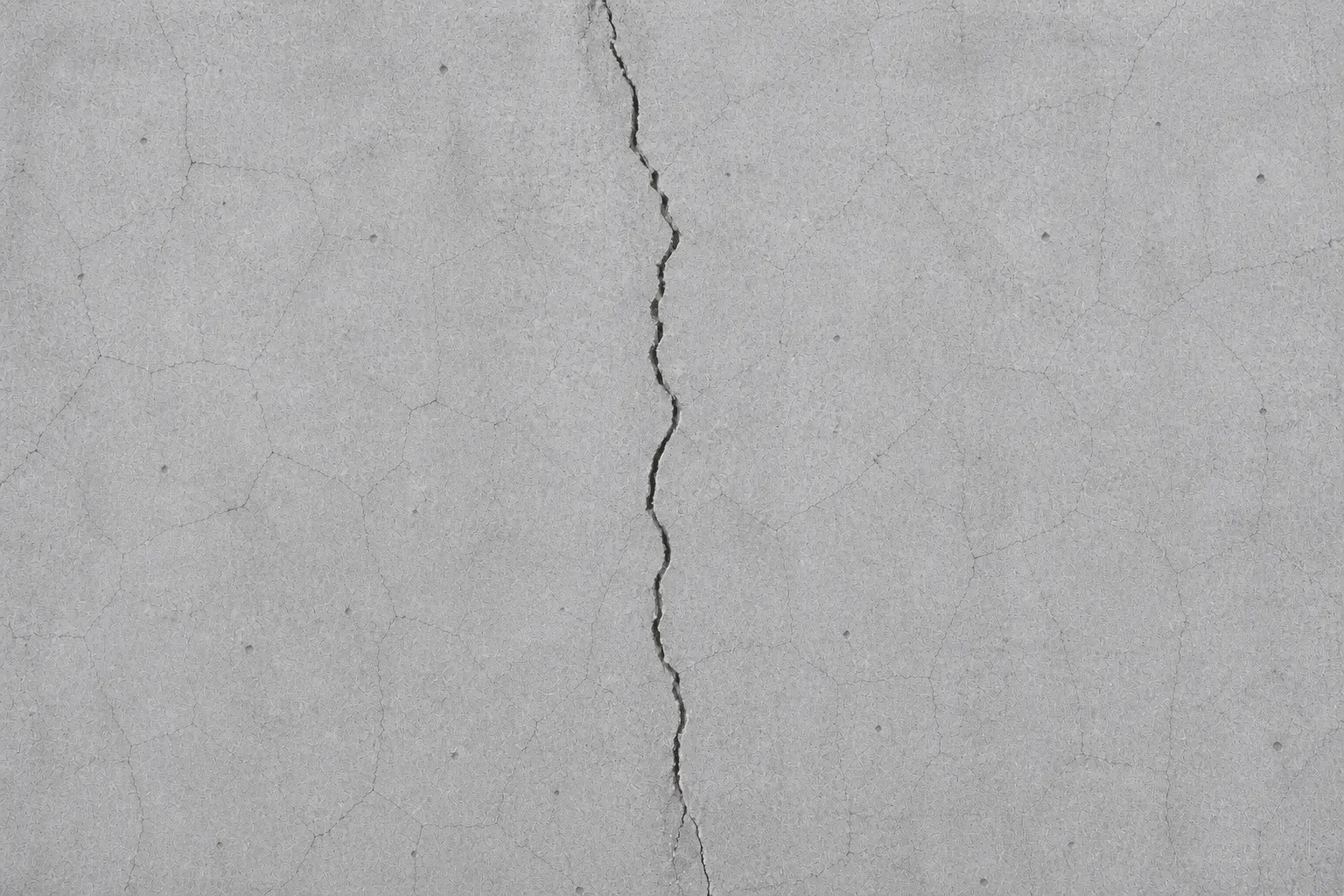 Betonwand mit einem ausgeprägten, vertikalen Riss in der Mitte und mehreren kleineren Haarrissen.
