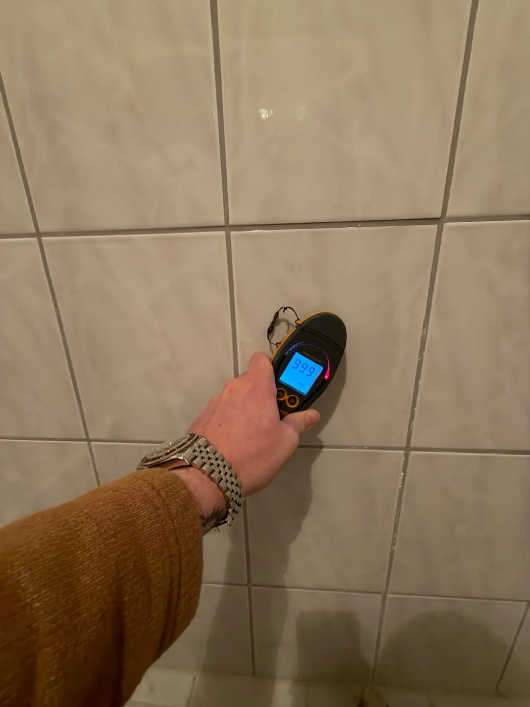 Feuchtemessgerät an einer gefliesten Badwand zeigt den Skalenendwert