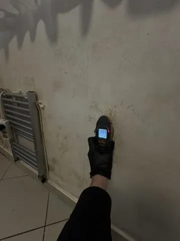 Feuchtemessgerät an einer fleckigen Wand neben dem Heizkörper